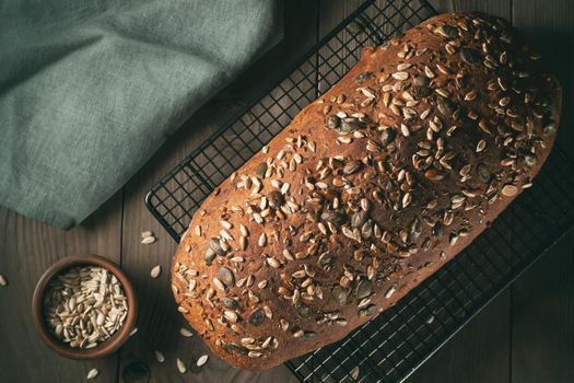 Loaf of homemade whole grain bread with seeds cool down on a wire rack on a wooden table.