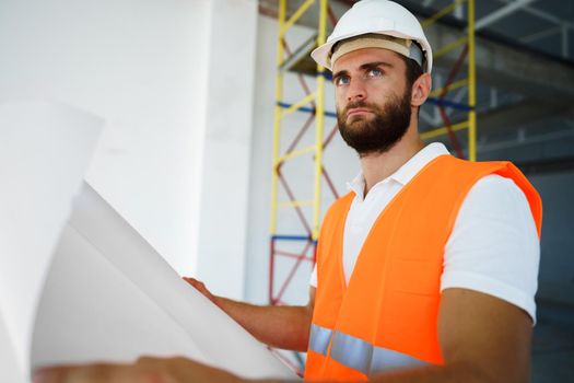 Builder or architect in hardhat supervising a project, looking at blueprints, close up