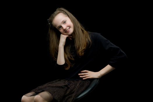 Girl teenager sitting on a chair in the studio on a black background. The concept of style and fashion.