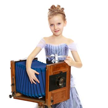 Adorable little blond girl dressed in long Princess dress.Girl posing near the big old camera.Isolated on white background.