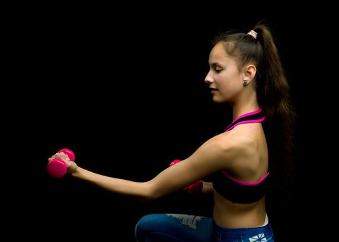 A teenage girl with dumbbells in her arms performs exercises in the fitness club. The concept of sport and a healthy lifestyle of the younger generation. Isolated