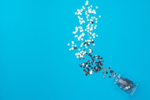Glass jar with scattered confetti on blue background top view