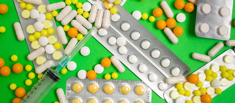colorful and white pills, capsules, syringe. Prevention, cure of influenza, coronavirus, covid-19. yellow, orange vitamins, tablets on green background. medical healthcare, protection concept banner