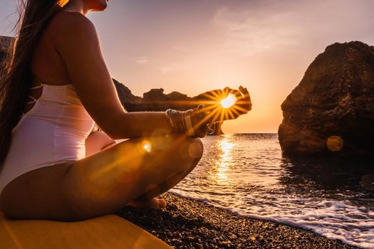 Young woman in swimsuit with long hair practicing stretching outdoors on yoga mat by the sea on a sunny day. Women's yoga fitness pilates routine. Healthy lifestyle, harmony and meditation concept.