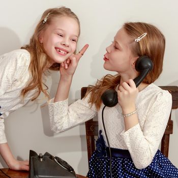 Two elegant girls sisters in beautiful dresses, talking on old phone. Retro style.Retro style.