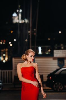 An elegant girl in a red evening dress on the streets of the night city of Marseille.A woman in a red evening dress in France.