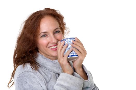 Smiling woman holding porcelain mug. Cheerful brown haired woman posing with cup of coffee or tea in her hands against white background. Female person enjoying of hot drink in the morning