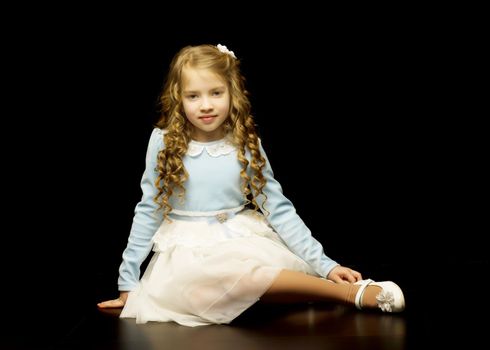 Beautiful little girl sitting in the studio on the floor on a black background. The concept of style and fashion.