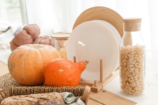 Kitchen countertop by the window in a bright room. Orange pumpkins, bread and pasta on the countertop. Autumn mood at home.