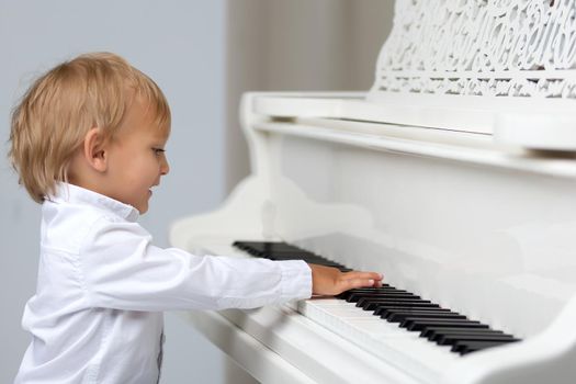 A cute little boy in a studio near a white grand piano. The concept of musical children's education, creative development of the child.