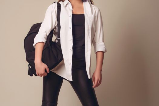 Beautiful blonde girl wearing a white shirt with a leather backpack on her back, on a gray background, shooting in the studio