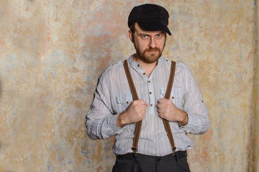 Happy groom. Portrait of handsome young man in white shirt and bow tie adjusting his suspenders and smiling at camera while standing isolated near old wall