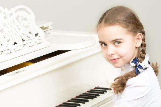 Charming little blonde with long wattled hair in plaits, playing on a white grand piano. In musical school.