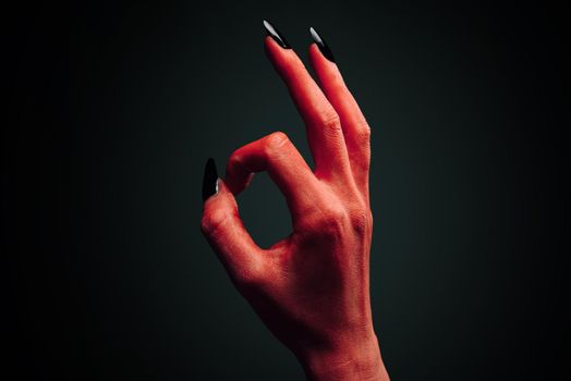 Red demon or devil hand with gesture OK on dark background. Halloween/horror theme