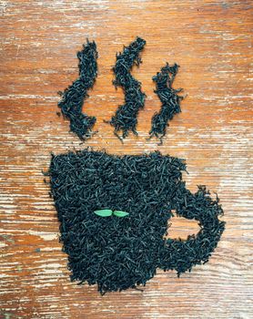 Black leaf tea in the shape of cup with green plant on a wooden table