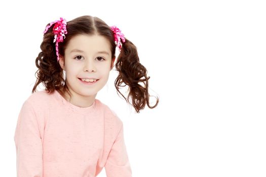 Beautiful little girl with long curly tails on the head,in which braided red ribbons . In long pink dress. The girl shyly sitting on the floor and straightens his arm hair. Close-up.Isolated on white background.