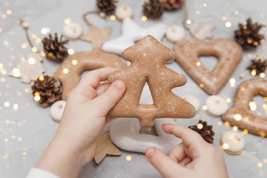 Children's hands hold a gingerbread in the shape of a Christmas tree. The concept of Christmas sweets, toys, garlands and bokeh. Decor for New Year holidays.