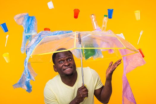 Plastic recycling problem, ecology and environmental disaster concept - Surprised african american man on yellow background with trash. He's worried about ecology disaster