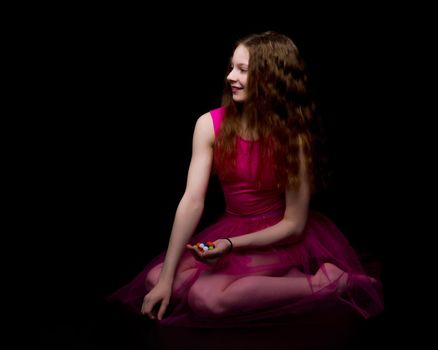 A beautiful little gymnast girl of school age holds multicolored confetti in her palms. Studio photography on a black background.