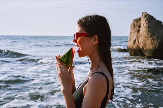woman in black swimsuit with watermelon by the ocean. High quality photo
