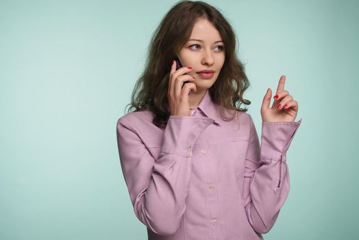beautiful caucasian surprised young girl talking on her cell phone pointing up isolated background - Image