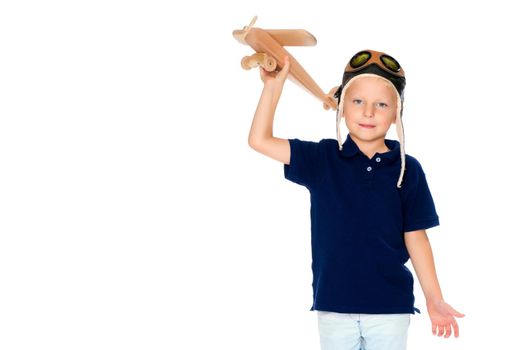 The boy in the helmet of the pilot plays with a toy wooden plane. He dreams of becoming a pilot. Concept of happy childhood, child in the family.Isolated on white background.