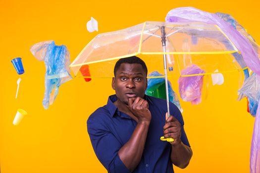 Problem of trash, plastic recycling, pollution and environmental concept - pensive african american man on yellow background with garbage