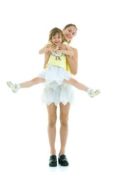 Beautiful young girl holding her little sister in her arms and looking at her with love. The concept of family happiness. Isolated on white background.