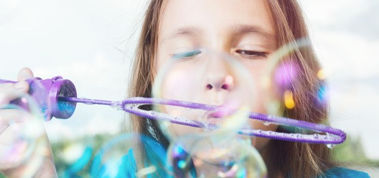 Portrait of little girl blowing soap bubbles on background of blue sky