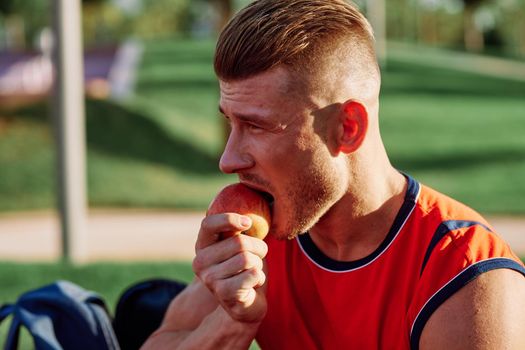 man in the park sits on a bench and eats an apple summer. High quality photo