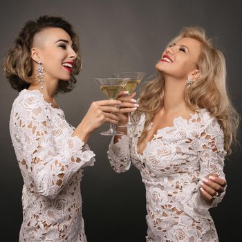 two beautiful young women girlfriends in white short dress celebrate the holiday with martini glasses isolated