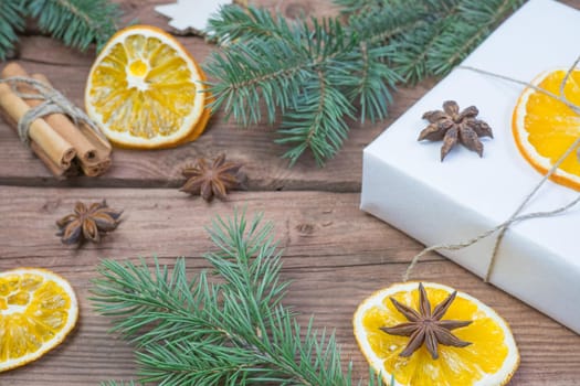 Christmas presents or gift box wrapped in kraft paper with decorations, pine cones, dry orange orange slices, cinnamon and fir branches on a rustic wooden background. Holiday concept
