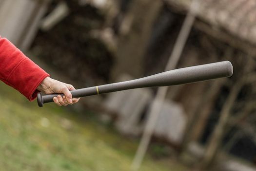 Woman's hand holds baseball bat in outdoor street.