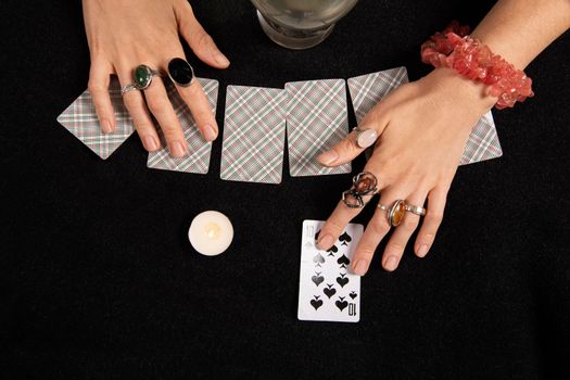 Fortune teller or witch hands, cards, candles and a glowing magic ball. Halloween, magic and tricks concept. Ten spades card