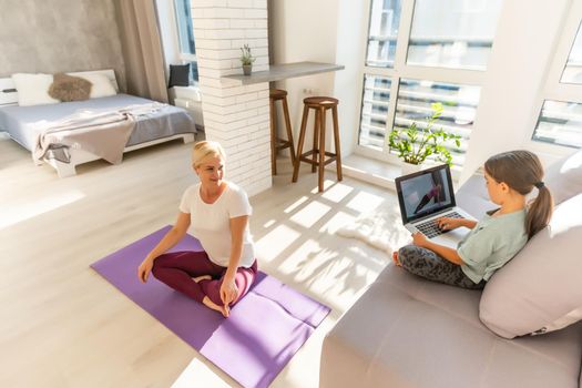 Young adult mother with her daughter watching online training together at home, looking a laptop