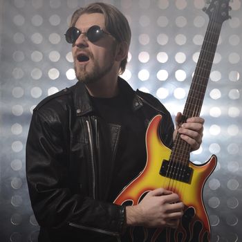 Attractive bearded man with glasses and black leather jackets plays guitar in smoke