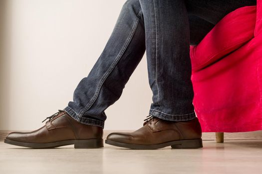 A man in stylish brown shoes sits on a red armchair - image