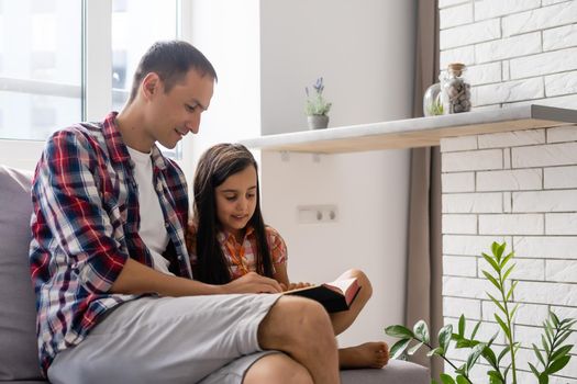 a young father with his little daughter reads the Bible