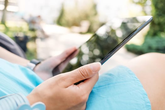 Unrecognizable young woman using digital tablet in the park, close-up of hands.