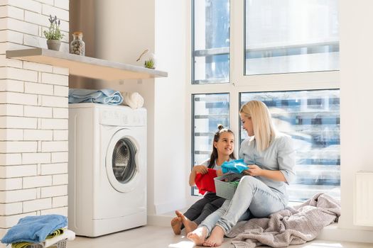 Young housewife and little girl doing laundry together