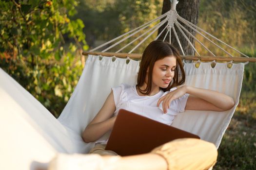 cheerful woman lies in a hammock with a laptop vacation internet travel. High quality photo