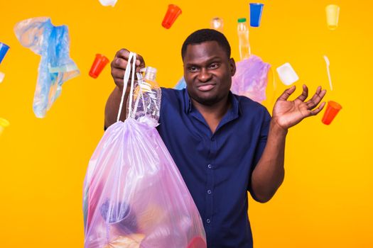 Problem of trash, plastic recycling, pollution and environmental concept - confused man carrying garbage bag on yellow background.