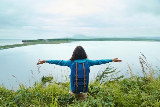 Free hiker young woman with her arms wide spread is enjoying in the summer day on nature, rear view