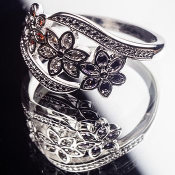 Silver Ring decorated with precious stones sapphire, cubic zirconia, ruby in the shape of flowers on a mirror surface