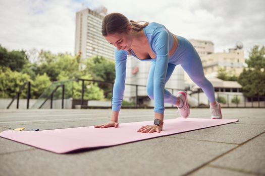 Beautiful fit caucasian woman is doing exercises outdoors at the city