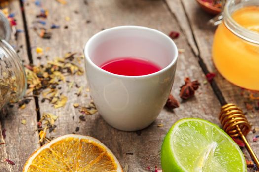 cups of healthy herbal tea with cinnamon, dried rose and camomile flowers in spoons over wooden background, top view
