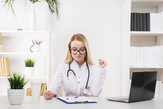 Young beautiful doctor woman working happy and smile in hospital, sitting on table, medical concept