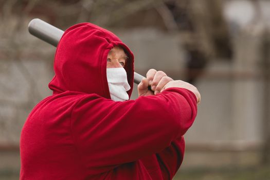 Angry aggressive elderly man in protective safe medical mask swings baseball bat in the background of outdoor street, portrait, close up.