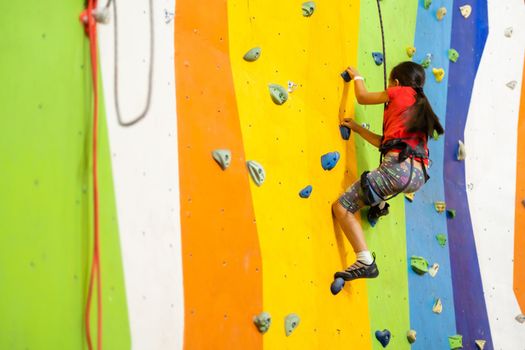 Sporty little girl climbing artificial boulder on practical wall in gym