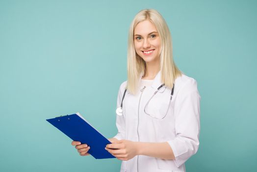 Portrait of an attractive young female doctor in white coat on blue background